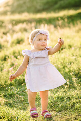 Child running in mountains on a summer day. Kid playing in spring sunlight outdoors. Toddler walks on green grass in field at sunset. Happy childhood. Beautiful cute girl walking in nature. Closeup.