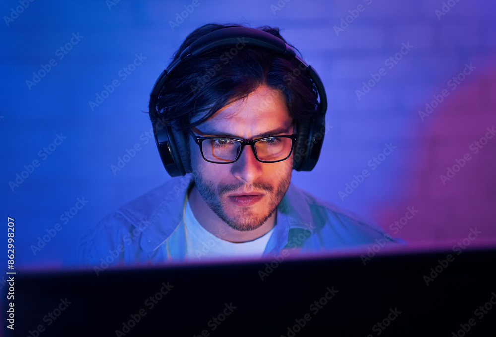Poster a young man wearing glasses and headphones sits in front of a computer screen in a dimly lit room. h