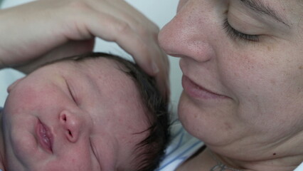 Cute newborn baby close-up face during initial days of life at hospital right after birth - mother...