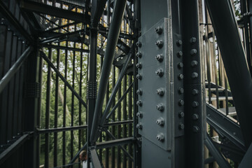 A detailed view of a bolted metal structure, showcasing the industrial design and engineering. The sturdy framework is surrounded by a natural backdrop of trees.