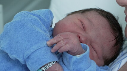 Cute newborn baby close-up face during initial days of life at hospital right after birth - mother hand caressing forehead bonding with infant, maternal care and motherhood concept