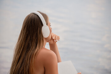 A woman wearing headphones is looking out at the water. The scene is calm and peaceful, with the...