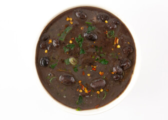 Black bean creamy soup with fresh herbs and pepper in white ceramic bowl white background