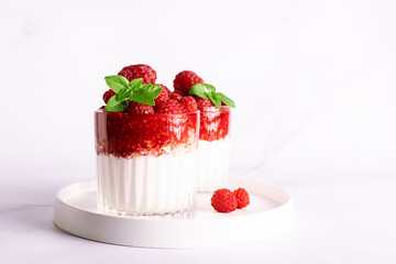 Tasty homemade yogurt parfait with granola, raspberry sauce, fresh raspberries and aromatic basil leaves in a glass on light marble background close up, healthy low carb dessert concept.