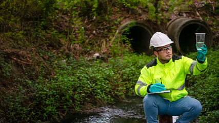 An ecologist in a green jacket sitting on a steel pole while holding the plastic glass on his left...