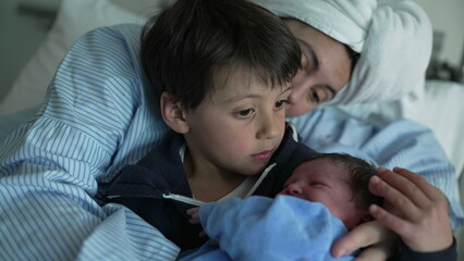 Tender Hospital Introduction of Newborn to Family - Young brother holds new baby while mother watches the siblings connect for the first time