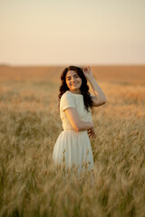 A young brunette walks in wheat fields at sunset in summer. Growing organic wheat and barley.