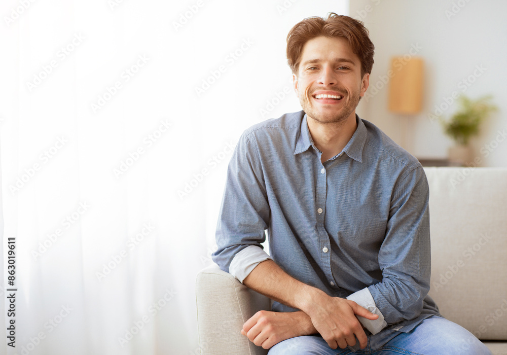 Poster cheerful man smiling at camera sitting on couch at home. empty space for text