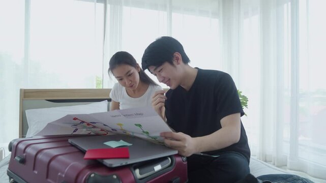 Two smiling friends are sitting with baggage. Cheerful couple exploring map on the bed in hotel.