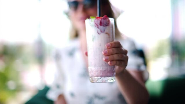 Woman presenting a strawberry drink with a black straw at a restaurant