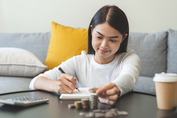 Financial, asian young woman, girl putting stack coins on table for calculate cost sitting in living room at home, financial plans to spend enough money on his income for saving money and payment.