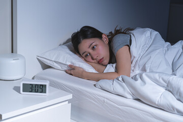 Annoyed, stressed, anxiety asian young woman suffering from insomnia with alarm clock time, frustrated awake on bed at night, health care problem, disturbed trouble of loud noise, unable sleepless.