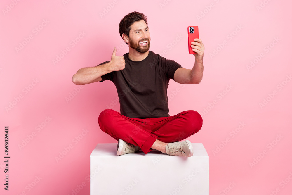 Poster full size photo of nice man dressed brown t-shirt sit on cube show thumb up make selfie on smartphon