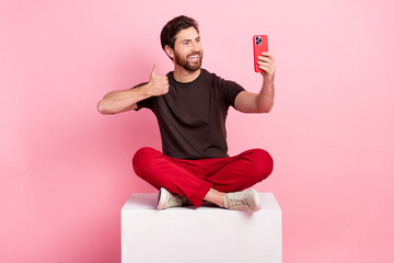 Full size photo of nice man dressed brown t-shirt sit on cube show thumb up make selfie on...