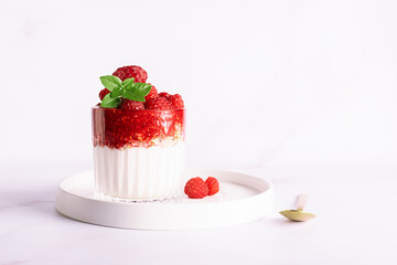Tasty homemade yogurt parfait with granola, raspberry sauce, fresh raspberries and aromatic basil leaves in a glass on light marble background close up, healthy low carb dessert concept.