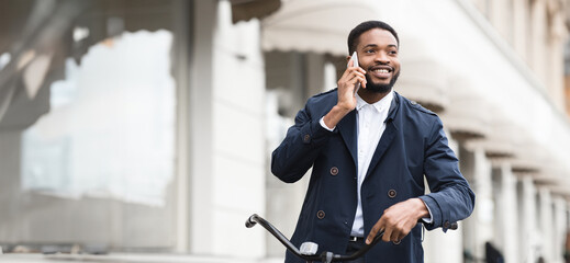 Black man is seated on his bike, talking on the phone outdoors. The mood is professional and active, highlighting the blend of work and personal time in a cityscape.