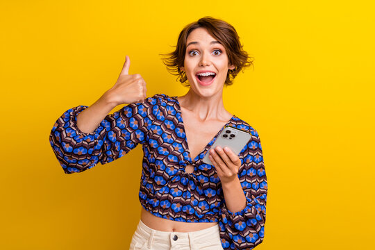 Photo of young girl vintage top showing thumb up respect symbol when download mindly app in cellphone isolated on yellow color background