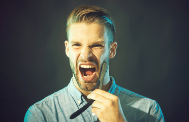 Barbershop. Professional hairdresser with straight razor. Angry barber with dangerous razor. Handsome screaming bearded man in denim shirt with classic old-fashioned sharp straight razor near beard.