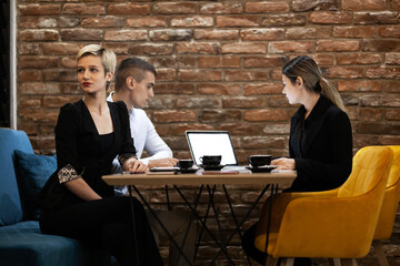 Three young professionals engage in a productive meeting at a cafe with laptops and coffee on...
