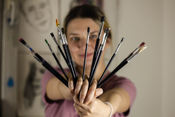 Artistic girl holding many dirty colorful used brushes with both hands.