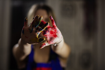 A creative female artist displays her colorful painted hands toward the camera, surrounded by a...