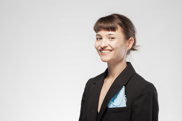 Cute girl in a suit with a mask in the pocket. Young business woman smiling.