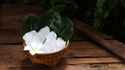 A basket filled with white alum crystals sits on a vibrant green shrub background.