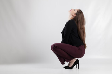 Young woman in stylish outfit freeing herself in a crouching pose against a white background