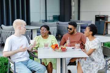 Group of multiethnic friends are enjoying cocktails and conversation at a sunny outdoor cafe in summer time