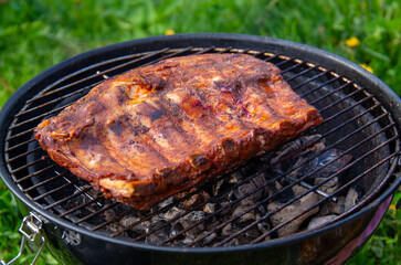 Mouthwatering Rack of Ribs on Round Grill in Backyard. Perfectly Glazed Barbecue Meat Sizzling Over Hot Coals