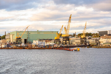 Fototapeta premium Quayside manufacturing plant with large yellow port cranes on the bank of a river at sunset in autumn