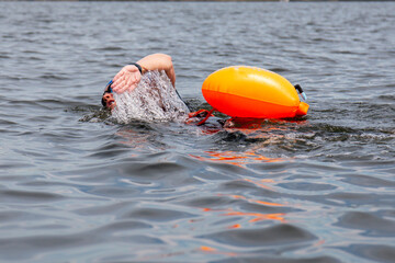 Close up of a women swimming in open water wearing an orange safety floatation