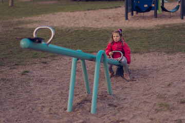 The girl is bored alone and has no one to ride with on the teeter-totter or seesaw and she sits on...