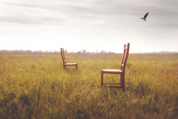 two abandoned chairs, one facing the other in the middle of a meadow, concept of waiting and love...