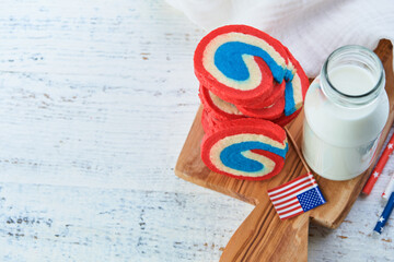 4th of July Holiday background. Red white and blue pinwheel sugar cookies with milk glass for July 4th celebration on old white wooden background. Patriotic American Flag Dessert Cookies for kids.