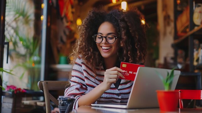 Cheerful positive young woman sitting at table at coffee shop holding red credit card and using modern laptop computer copy space Online shopping banking ecommerce concept : Generative AI