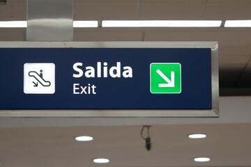 Blue exit signboard at an airport, written in spanish and english.