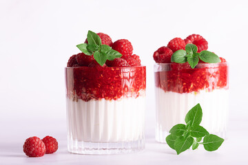  Tasty homemade yogurt parfait with granola, raspberry sauce, fresh raspberries and aromatic basil leaves in a glass on white marble background close up, healthy low carb dessert concept.
