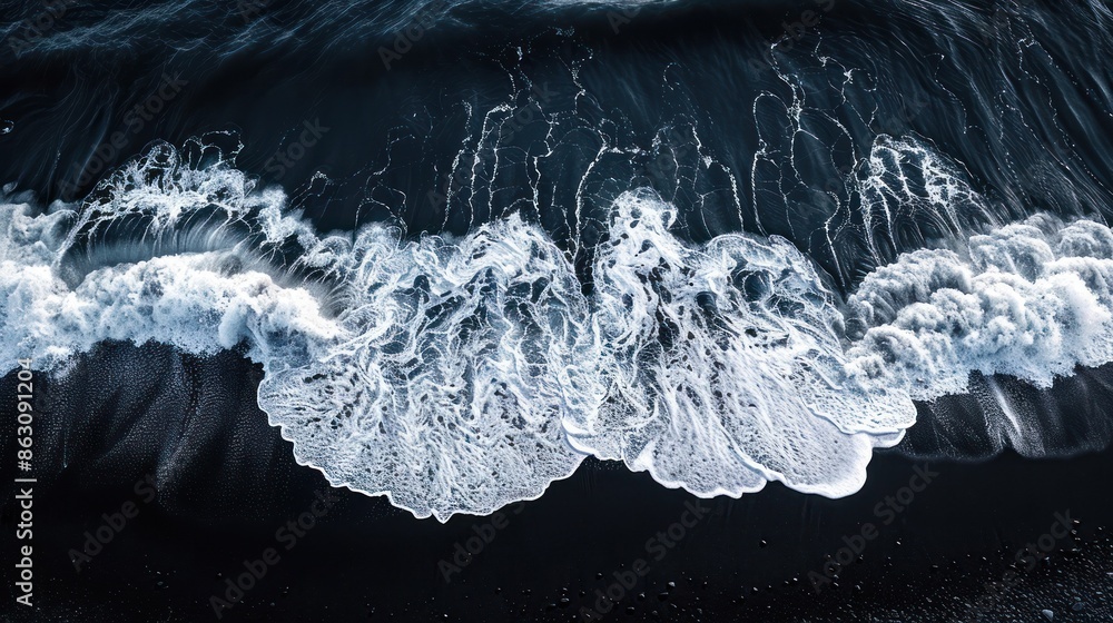 Wall mural Aerial view of white ocean waves crashing on a dark sandy beach capturing the natural contrast of sea foam and black sand. - Wall murals