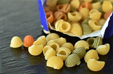 dry healthy pasta made from spinach  ,tomaten and wheat scattered from a paper bag