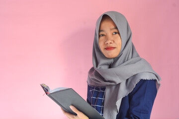 Portrait of Asian woman reading a book on isolated pink background