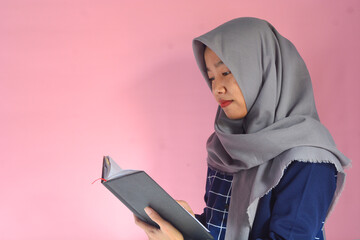 Portrait of Asian woman reading a book on isolated pink background