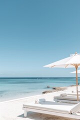 Summer concept of umbrellas and wooden deckchairs on a white sandy beach with a view of the blue sea and clear sky.
