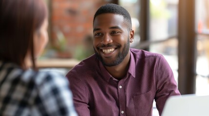 Fototapeta premium Man smiling during a conversation in an office setting, with a laptop, suggesting a professional discussion.