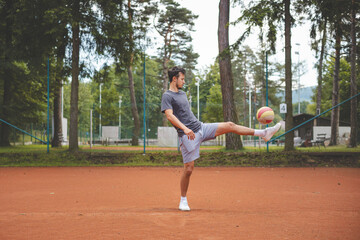 Soccer player in 20s plays with a balloon on a clay court. Amateur sport. Individual football training. Soccer. Kicking, striking, passing and dribbling