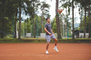 Soccer player in 20s plays with a balloon on a clay court. Amateur sport. Individual football training. Soccer. Kicking, striking, passing and dribbling