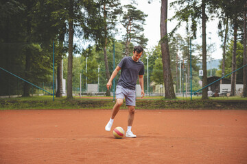 Soccer player in 20s plays with a balloon on a clay court. Amateur sport. Individual football...