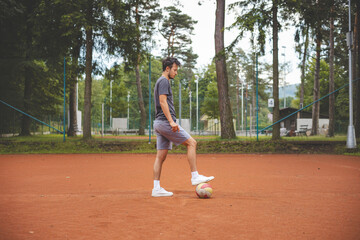 Soccer player in 20s plays with a balloon on a clay court. Amateur sport. Individual football training. Soccer. Kicking, striking, passing and dribbling