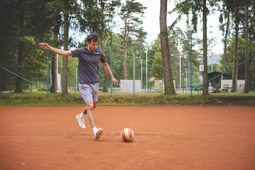 Soccer player in 20s plays with a balloon on a clay court. Amateur sport. Individual football training. Soccer. Kicking, striking, passing and dribbling