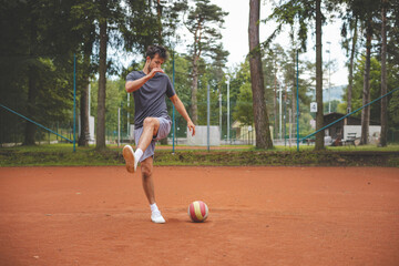 Soccer player in 20s plays with a balloon on a clay court. Amateur sport. Individual football training. Soccer. Kicking, striking, passing and dribbling